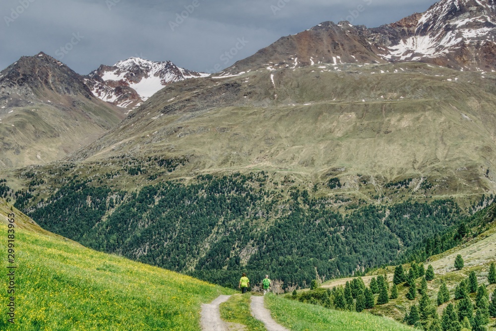 couple wandering a mountain path in the Alps, sunny summer day overlooking the lush nature, hills, meadows and forests