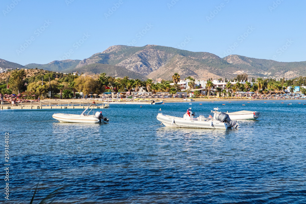 Beautiful bay with blue water, sandy beach and boats. Small town and green mountains on the coast of the Aegean sea