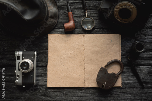 Open blank page detective book with various equipment around on black wooden table background.