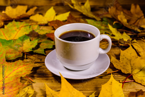 Cup of coffee and heap of yellow maple leaves on a wooden table