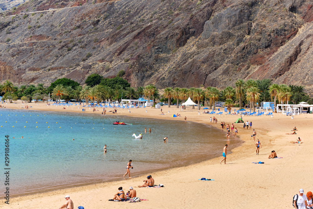 People sunbath on sandy picturesque cozy beach of Playa de Las Teresitas, enjoy views and warm weather and Atlantic  Ocean waters, Tenerife, Canary Islands, Spain