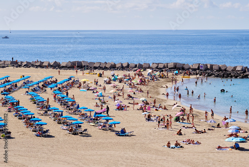 Vacationers people sunbathing on sandy beach of Playa de los Cristianos, enjoy warm Atlantic Ocean waters, Tenerife, Canary Islands, Spain