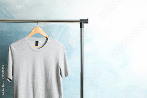 Rack with blank gray t-shirt on blue background, space for text