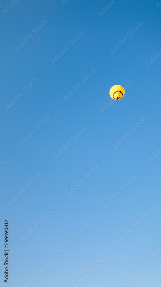 Yellow air balloon flying far away in the clear blue sky of Cappadocia, Turkey.  