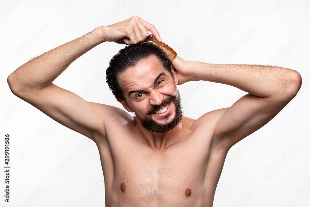 Stylish handsome bearded with mustaches have problems combing his hair standning bare isolated over white background. Concept of morning treatment.
