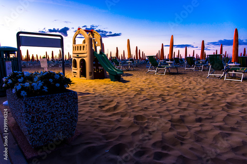 Slide for children on the beach with sunbeds in the background at sunrise time. Jesolo beach, Italy.