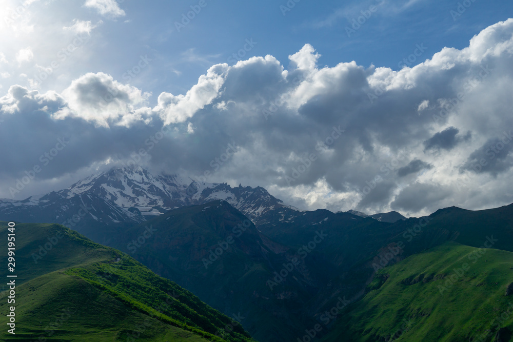 Landscape mountain view peaks in snow and green hills, deep blue sky and huge white clouds background, Caucasian mountains, Kazbek mountain Landscape mountain view peaks in snow and green hills, deep blue sky and huge white clouds background, Caucasian mountains, Kazbek mountain