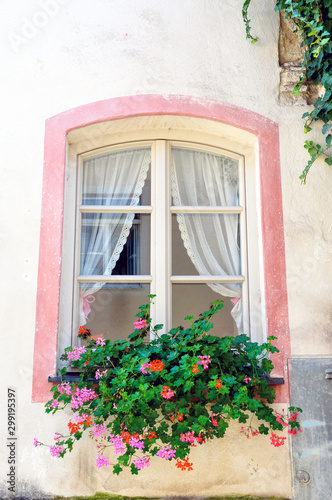 A beautiful pink framed window with lace curtains shows flowers in a planter box.