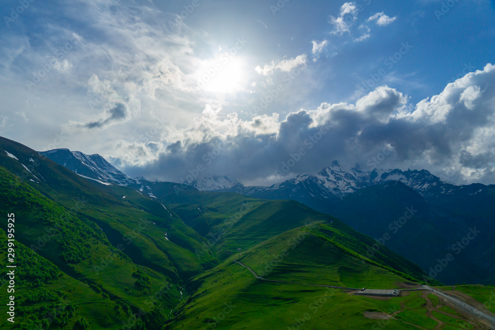 Landscape mountain view peaks in snow and green hills, deep blue sky and huge white clouds background, Caucasian mountains, Kazbek mountain