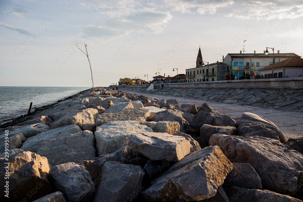 Stone shore with view at the sea on the left and at the town on the right. Caorle, Italy.