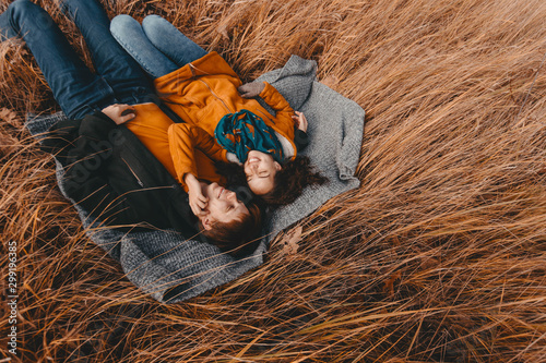 Young man and woman are lying and hugging on a plaid in an autumn field. Romance, traveling together, harmony, family happiness, a date in nature.