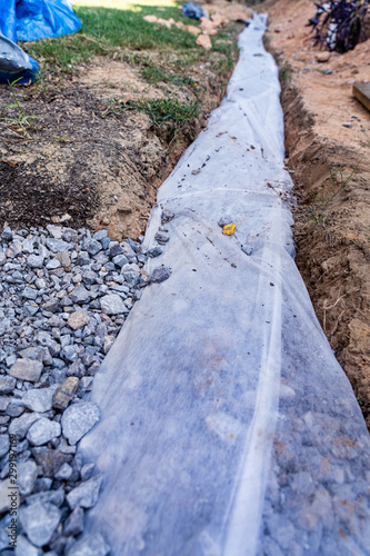 Fabric covers drainage rock and pipe to keep a French drain clear of debris in this DIY home improvement project to alleviate drainage issues.