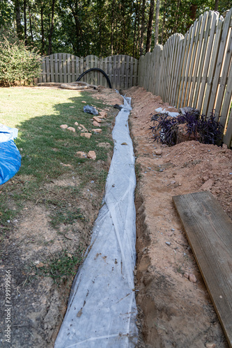 Fabric covers drainage rock and pipe to keep a French drain clear of debris in this DIY home improvement project to alleviate drainage issues.