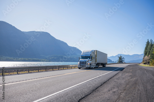 Big rig professional popular semi truck tor long haul freight transporting cargo in refrigerator semi trailer running on the road along the Columbia River at sunny day