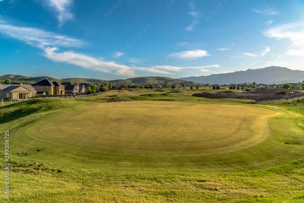 Scenic golf course landscape against houses and mountain under sky and clouds