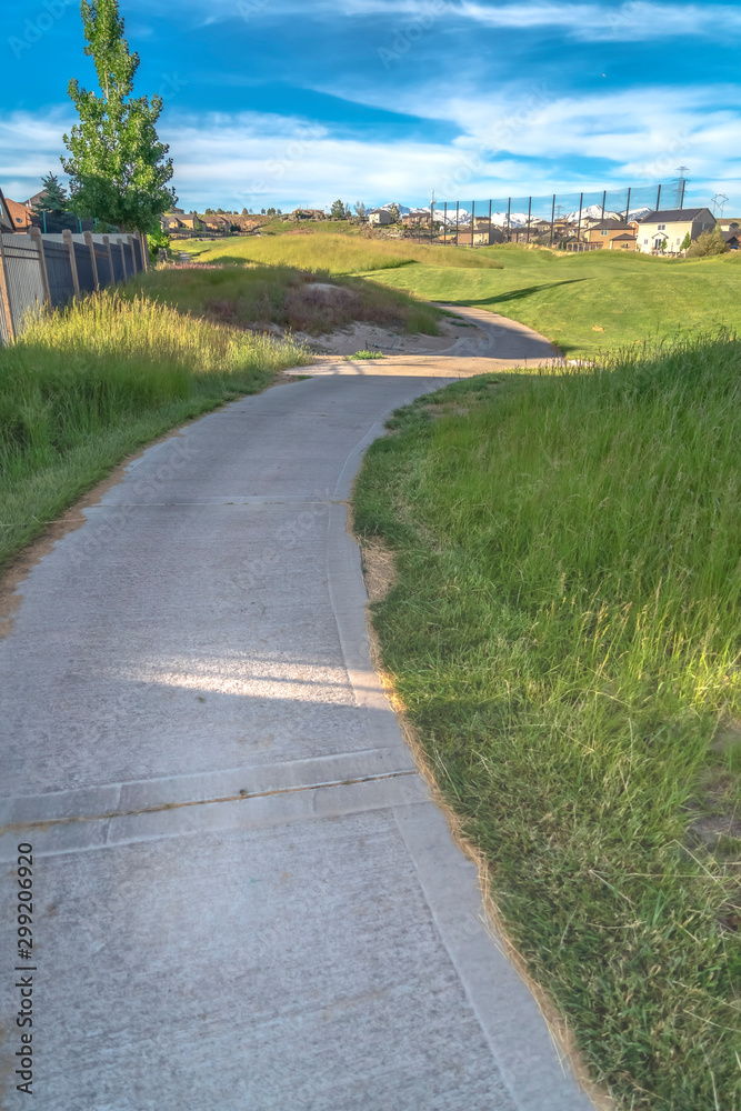 Pathway amid grasses leading to a golf course with houses in the distance