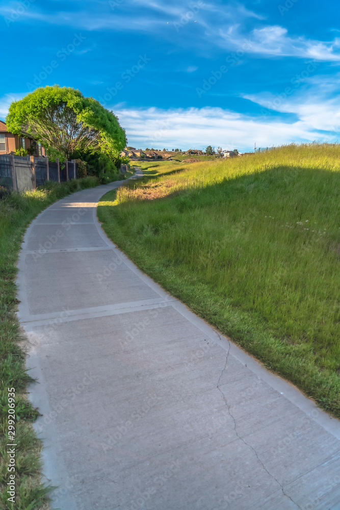 Concrete pathway on a grass covered hill under blue sky on a sunny day