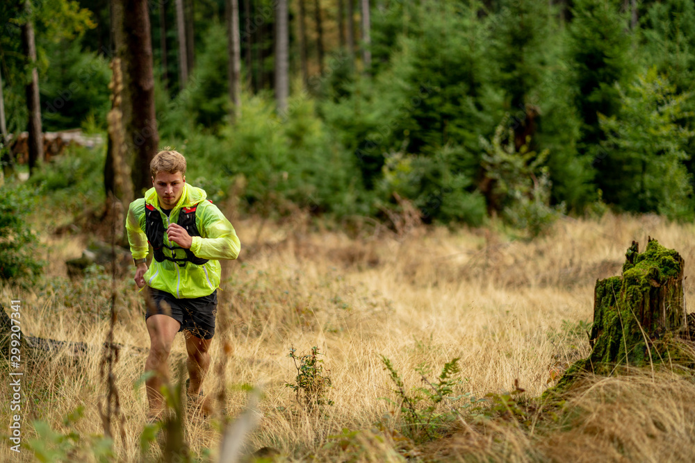 Young athlete runs uphill with a drinking backpack. Trail run in a beautiful autumn forest