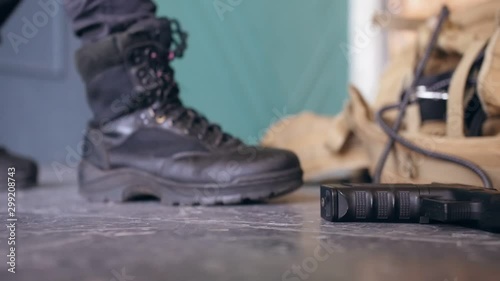 A soldier picks up a pistol and military bag from the floor and walks away. Shooting from below. Сlose up shot.