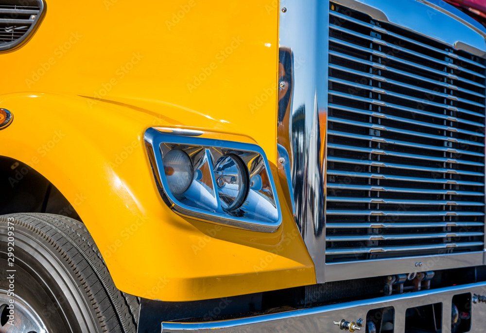 Part of yellow big rig semi truck with chrome grille and headlight with reflection of sunlight - obrazy, fototapety, plakaty 