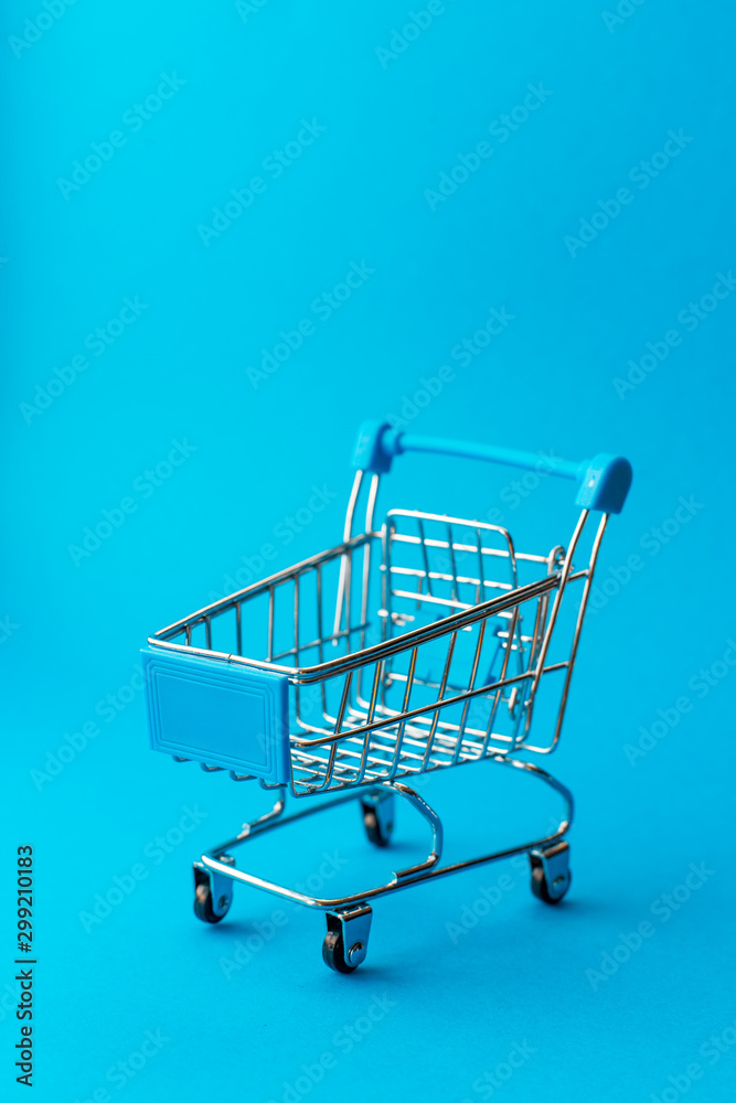 empty metal shopping trolley on blue background. Discount and shopping concept