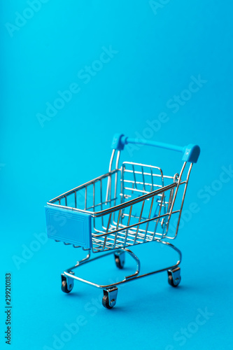 empty metal shopping trolley on blue background. Discount and shopping concept
