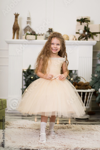 Little cute girl princess in a chic dress laughs and poses near the Christmas tree