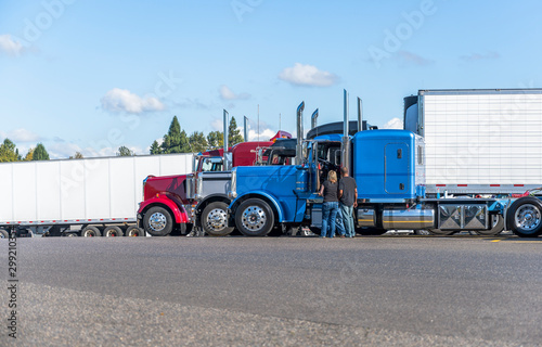 Truck drivers exchange views on the strengths and weaknesses of their big rigs semi trucks standing on truck stop