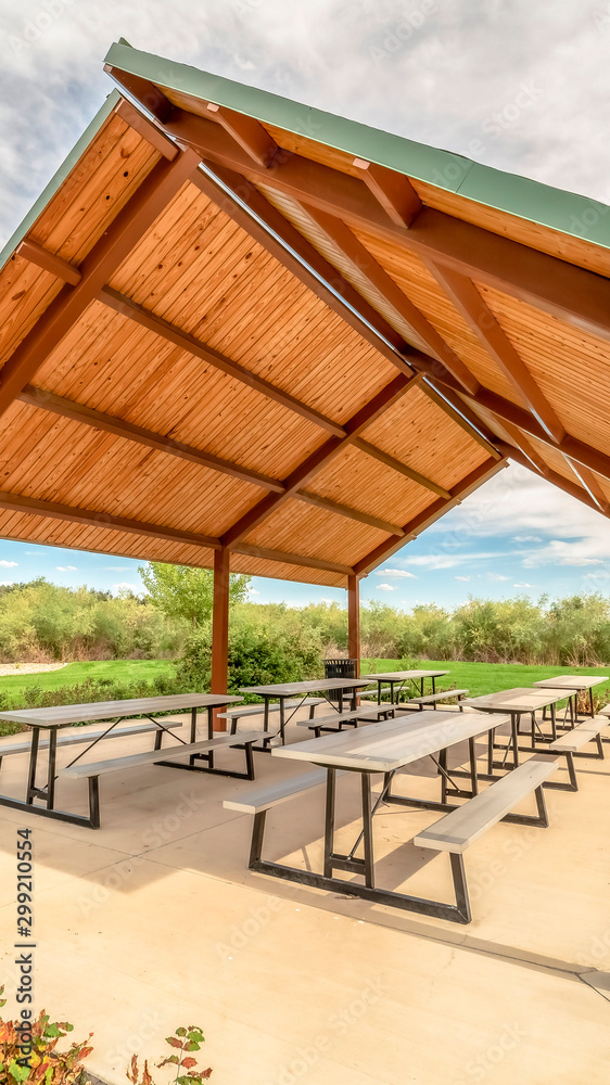 Vertical Sunny day at a park with view of tables and benches under a picnic pavilion