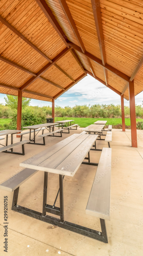 Vertical Row of white tables with seats under a pavilion with brown ceiling at a park