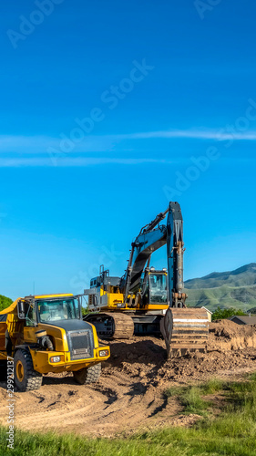 Vertical frame Truck and excavator at a construction site with blue sky overhead on a sunny day