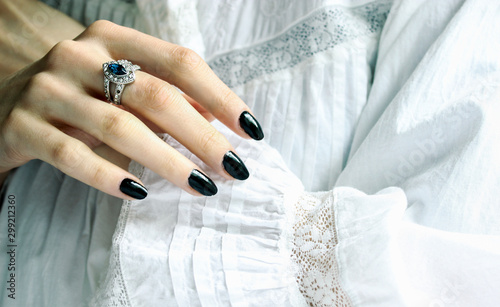 Woman's hand with black nail varnish/polish wearing a silver ring with blue gem stone