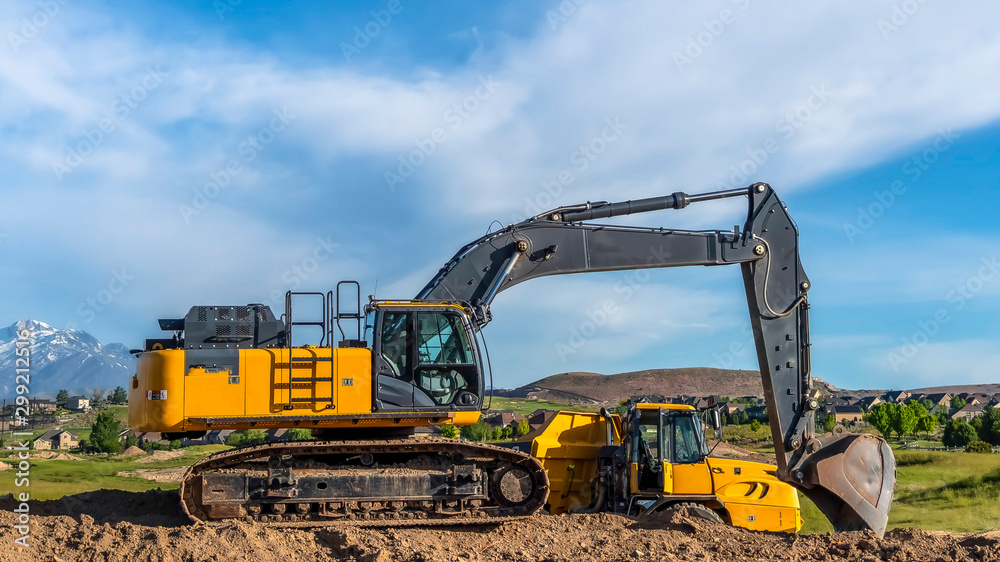 Panorama Excavator at a construction site with mountain homes and cloudy sky background Panorama Excavator at a construction site with mountain homes and cloudy sky background