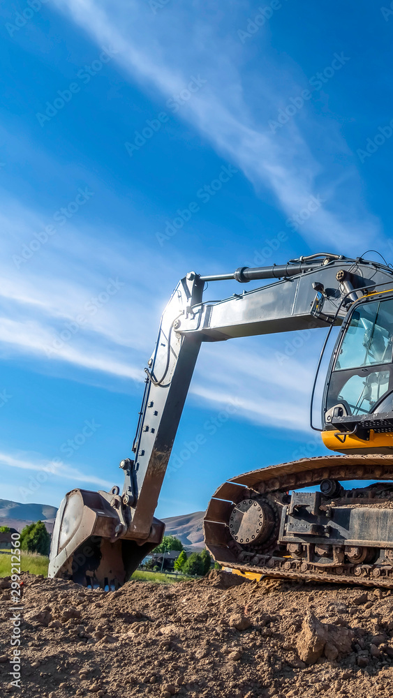 Obraz premium Vertical Yellow excavator with continuous tracks digging soil at a construction site