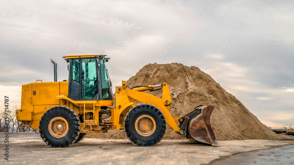 Panorama Bulldozer in front of a mound of soil with leafless trees and cloudy sky background Panorama Bulldozer in front of a mound of soil with leafless trees and cloudy sky background