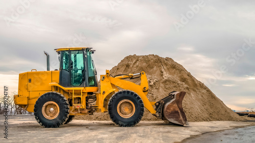 Panorama Bulldozer in front of a mound of soil with leafless trees and cloudy sky background