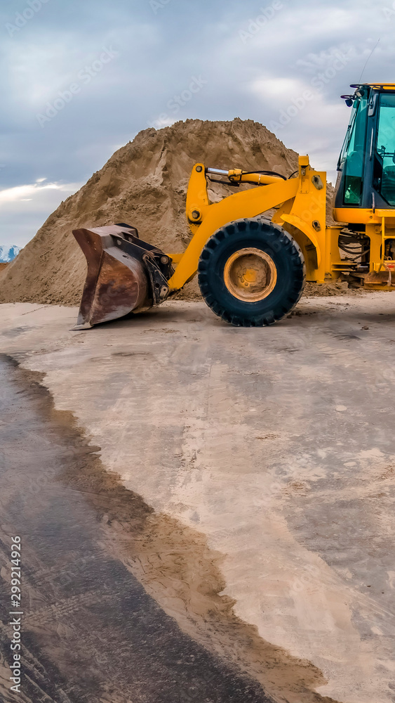 Obraz premium Vertical Yellow bulldozer on a road with mound of soil and cloudy sky background
