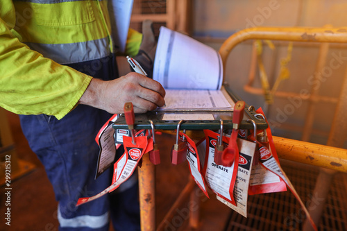 Personnel red locks attached with danger tag together with safety isolation permit lock box supervisor permit holder checking wring  co- worker names sign on sheet at the back ground 
