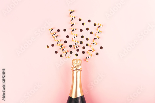 Creative New Year composition with champagne bottle and exploding gold confetti and streamers. Celebration and party concept.