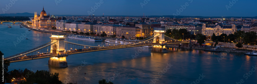 Panorama of Budapest along the Danube River featuring the Chain Bridge and Hungarian Parliament Building at blue hour. 