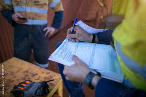 Construction co-worker checking site emergency phone number on cell phone while supervisor whitening on working at height permit prior to performing high risk work construction site open field