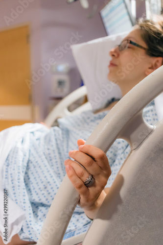 mother in hospital bed pregnant and in labor  holding on to bed rail in pain  wedding rings showing