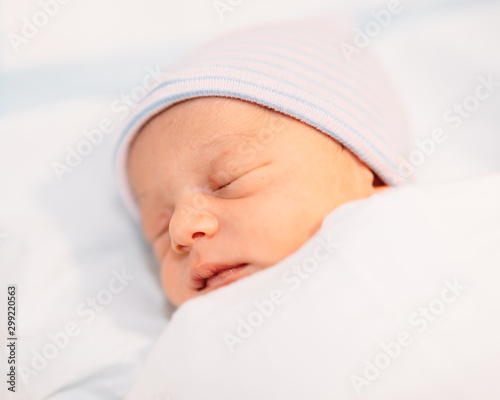 sleeping newborn baby boy in a wrap on white blanket