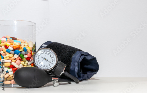 clear container full of different colored medical therapeutic drugs, pills, capsules and tablets, and a sphygmomanometer. hypertension control concept. health care  or health neglect concept.