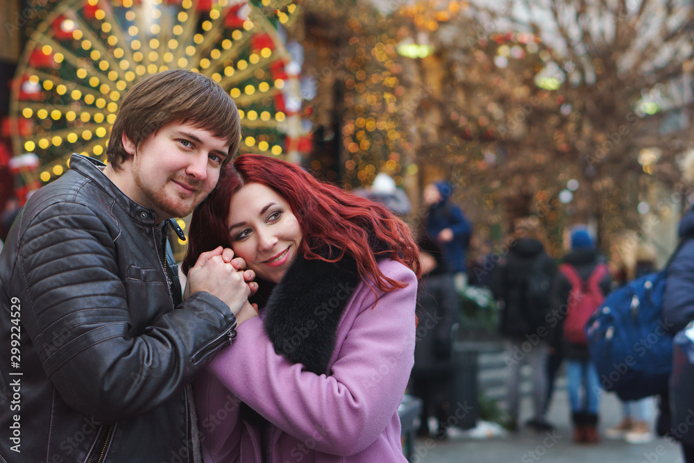 Loving couple in festive Christmas city celebrate the New Year. Romantic walk in winter. Having fun in winter christmas fair market decorations at central square city. Vacation and holiday concept