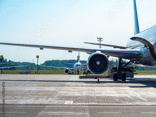 Barcelona, Spain - august 2019: middle distance view on airplanes standing on asphalt takeoff runway. Line of green trees on background. Selective soft focus. Blurred background