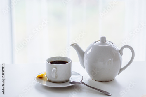 white cuo and white teapot on the white table with black tea and fresh lemon