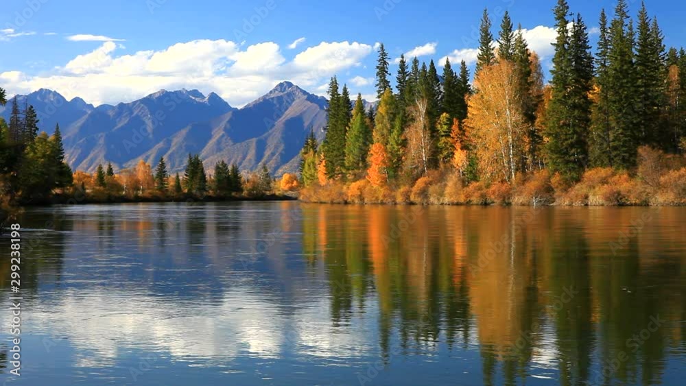 Tranquil autumn landscape with a reflection of yellowed trees and a mountain range in the Irkut River on a sunny day. Siberia, Baikal region, Eastern Sayan Mountains,  Buryatia, Tunka valley