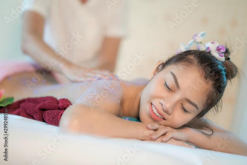 Young Asian woman receiving salt massage in spa salon, Hand putting salt scrub on female back, Spa concept