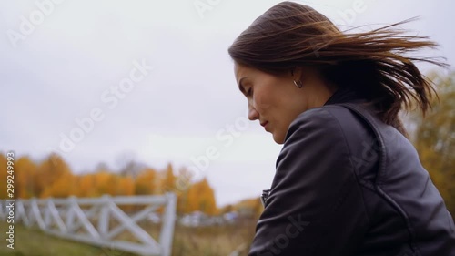 A girl in a black leather jacket is walking in the cool, windy weather outside. Her hair develops in the wind